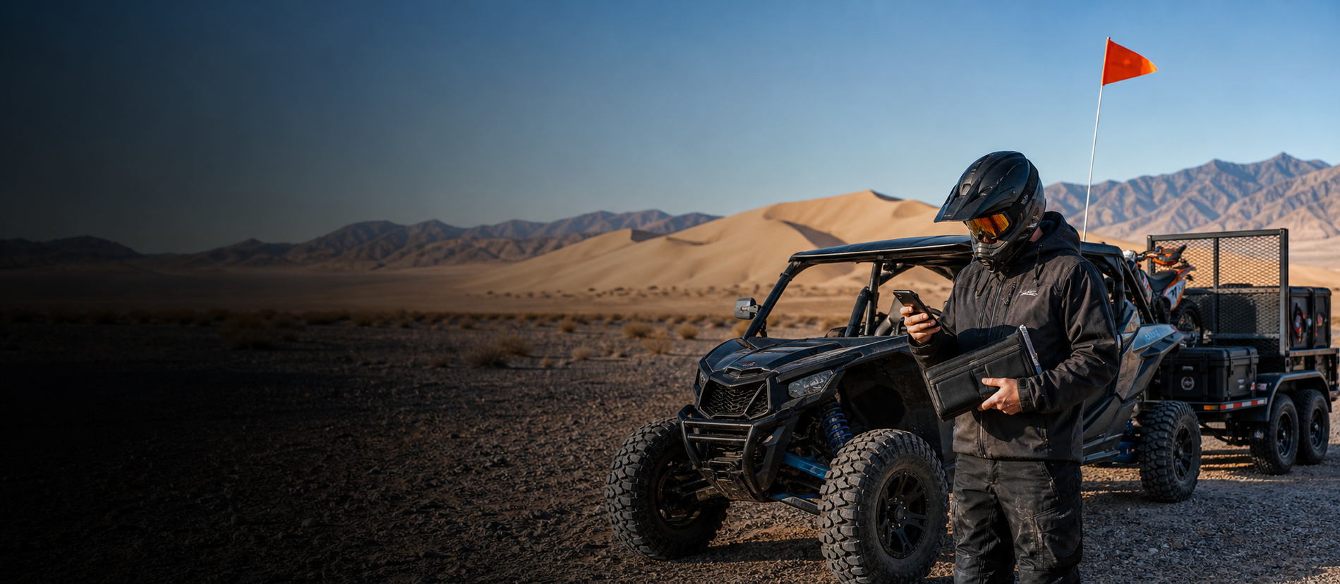A prepared rider checking an electronic pass beside a flagged side-by-side at Sand Mountain