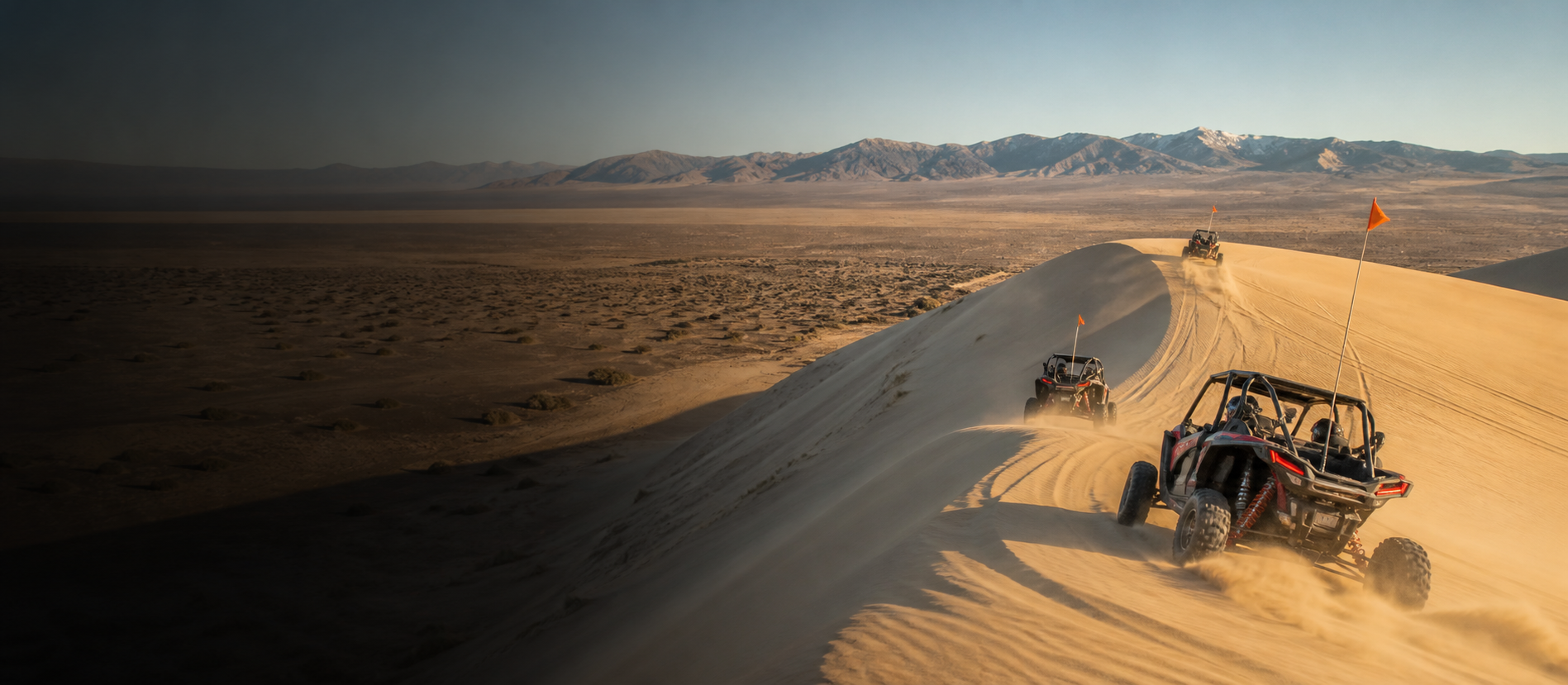 A spaced group of side-by-sides with orange whip flags riding a Sand Mountain dune ridge